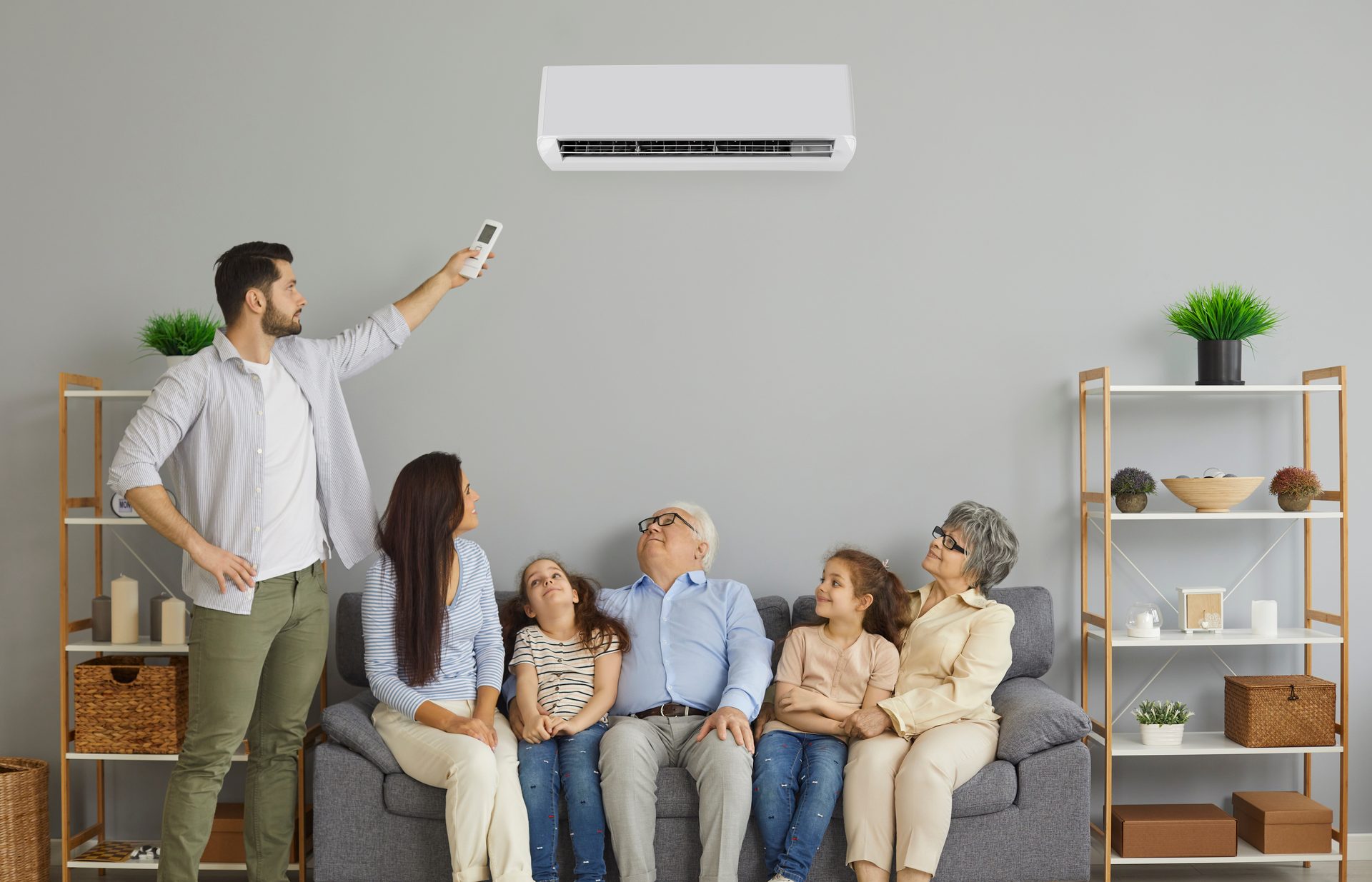 Family relaxing on a couch while a man adjusts a split system air conditioner with a remote