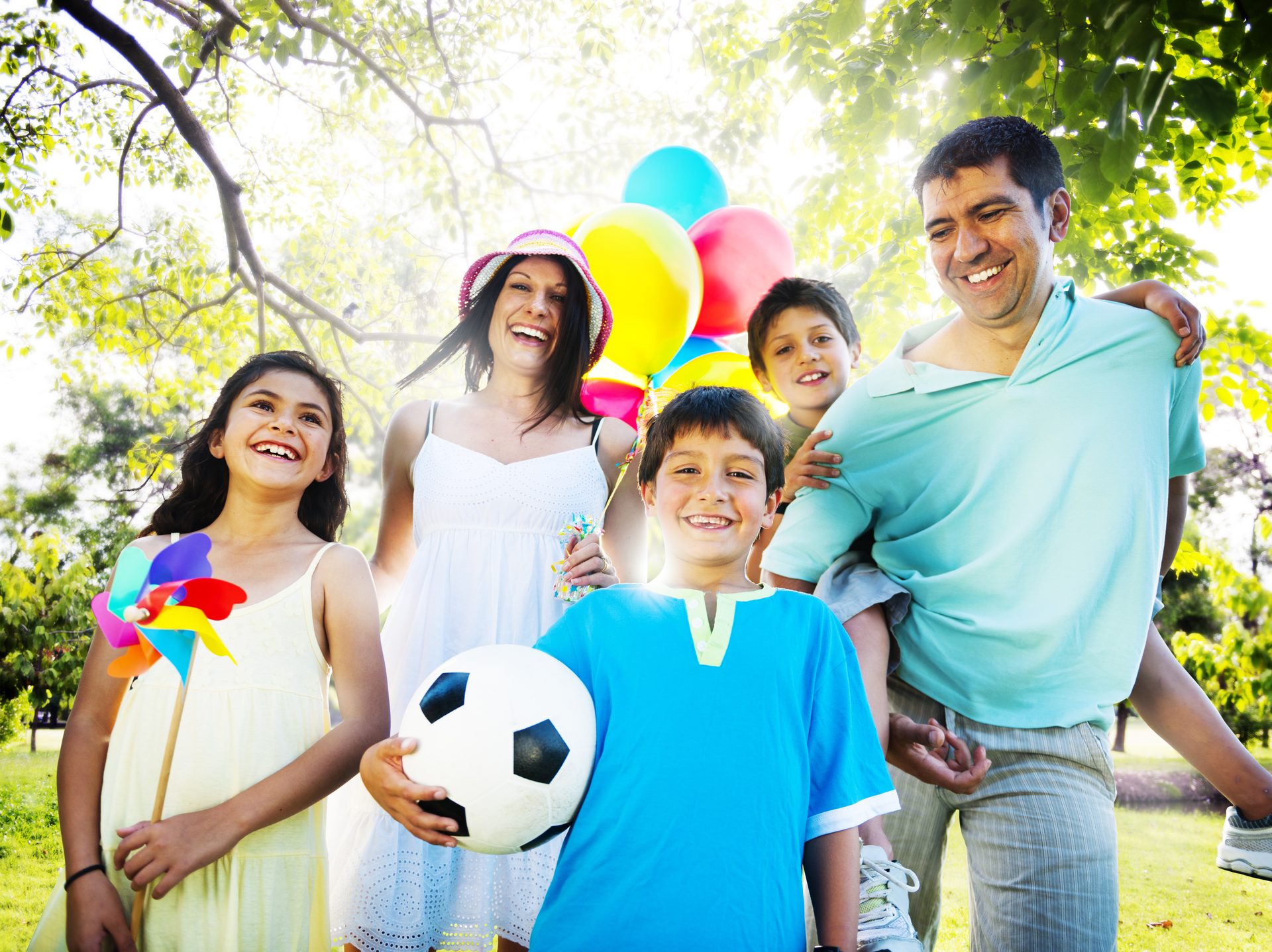 Smiling family with balloons and a soccer ball enjoying a sunny day out in the park